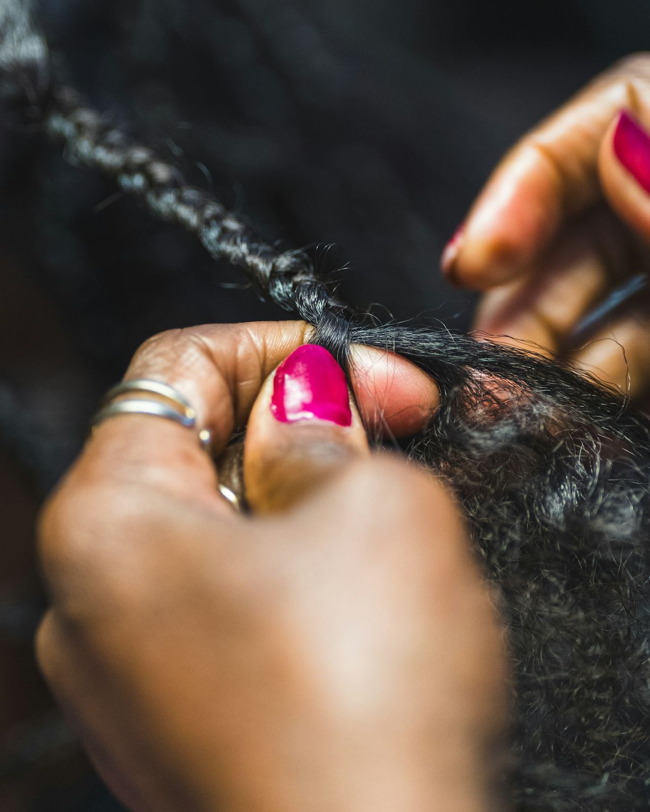 Hands with bright pink nails braiding hair