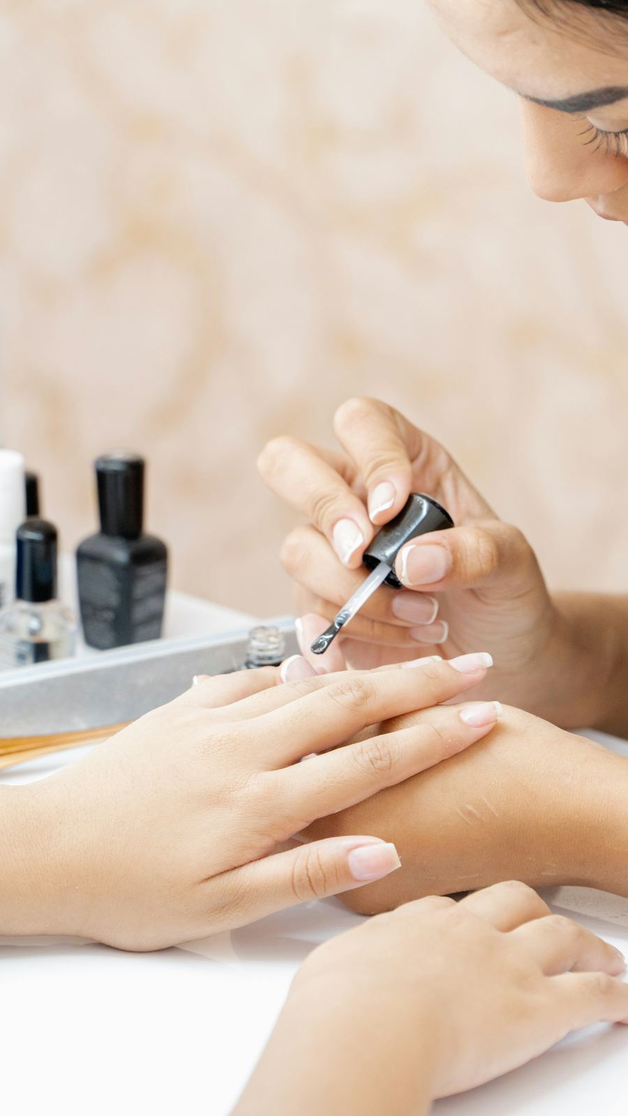 A nail technician painting a client's nails with clear polish
