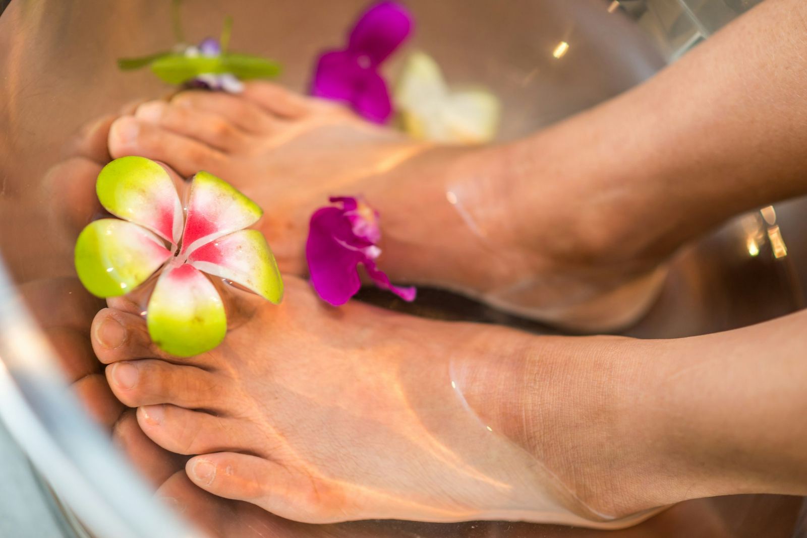Feet resting in a warm foot bath scattered with flowers