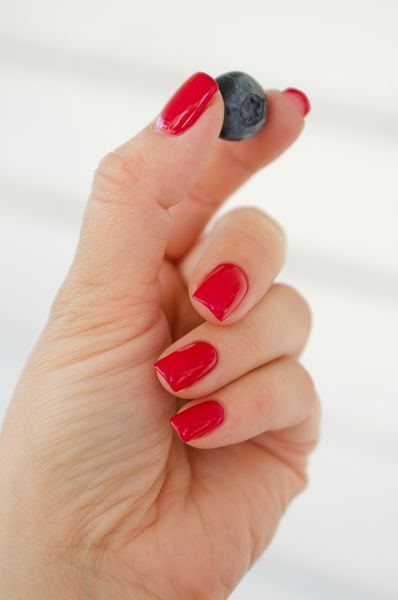 Classic glossy red nails holding a blueberry