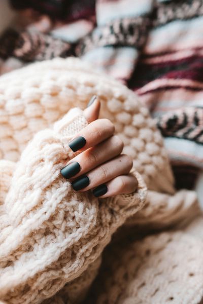 Deep forest green nails against a cream knit sweater