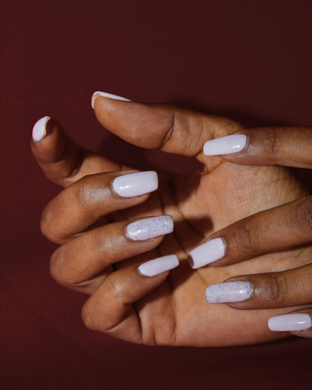 Hands with milky white gel nails against a deep red background