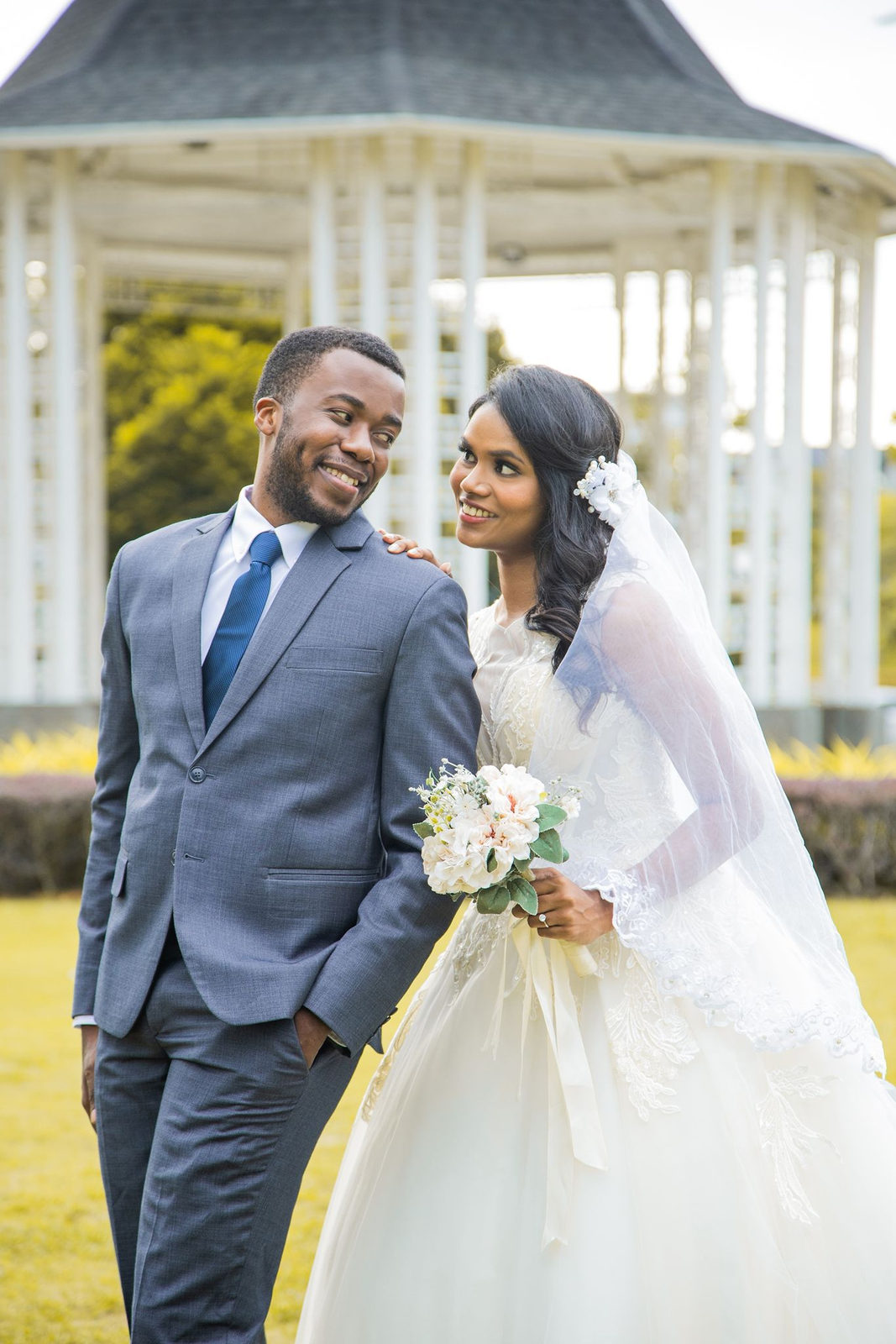 Munshya and Aghalya in wedding attire, smiling at each other in front of a white gazebo