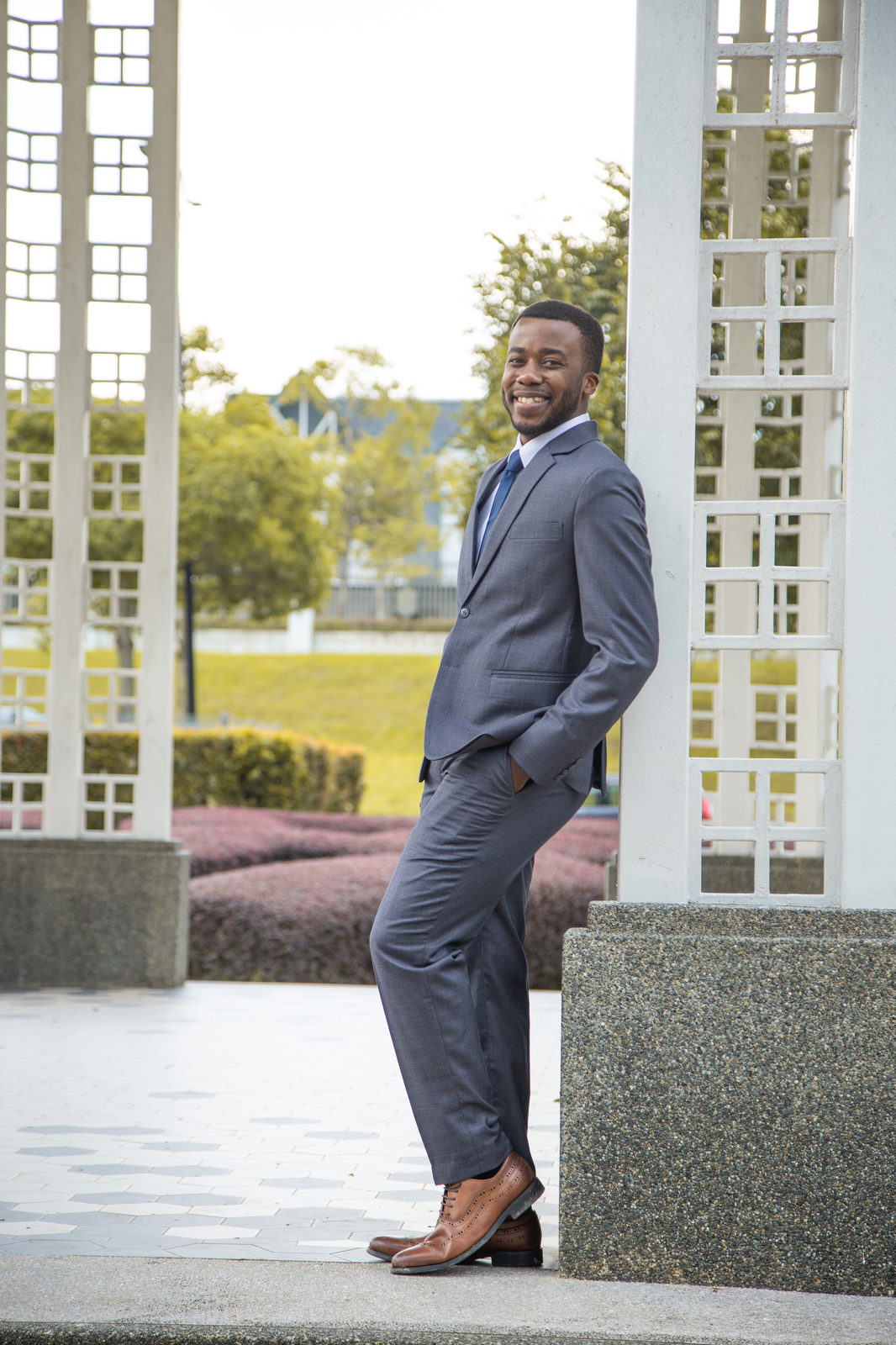Munshya in a grey suit leaning against a pergola pillar