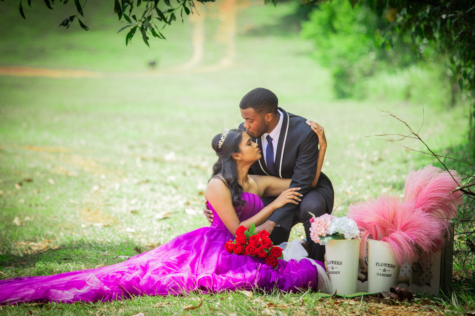 Munshya kissing Aghalya's forehead as they sit on the grass beside red roses and pink pampas grass