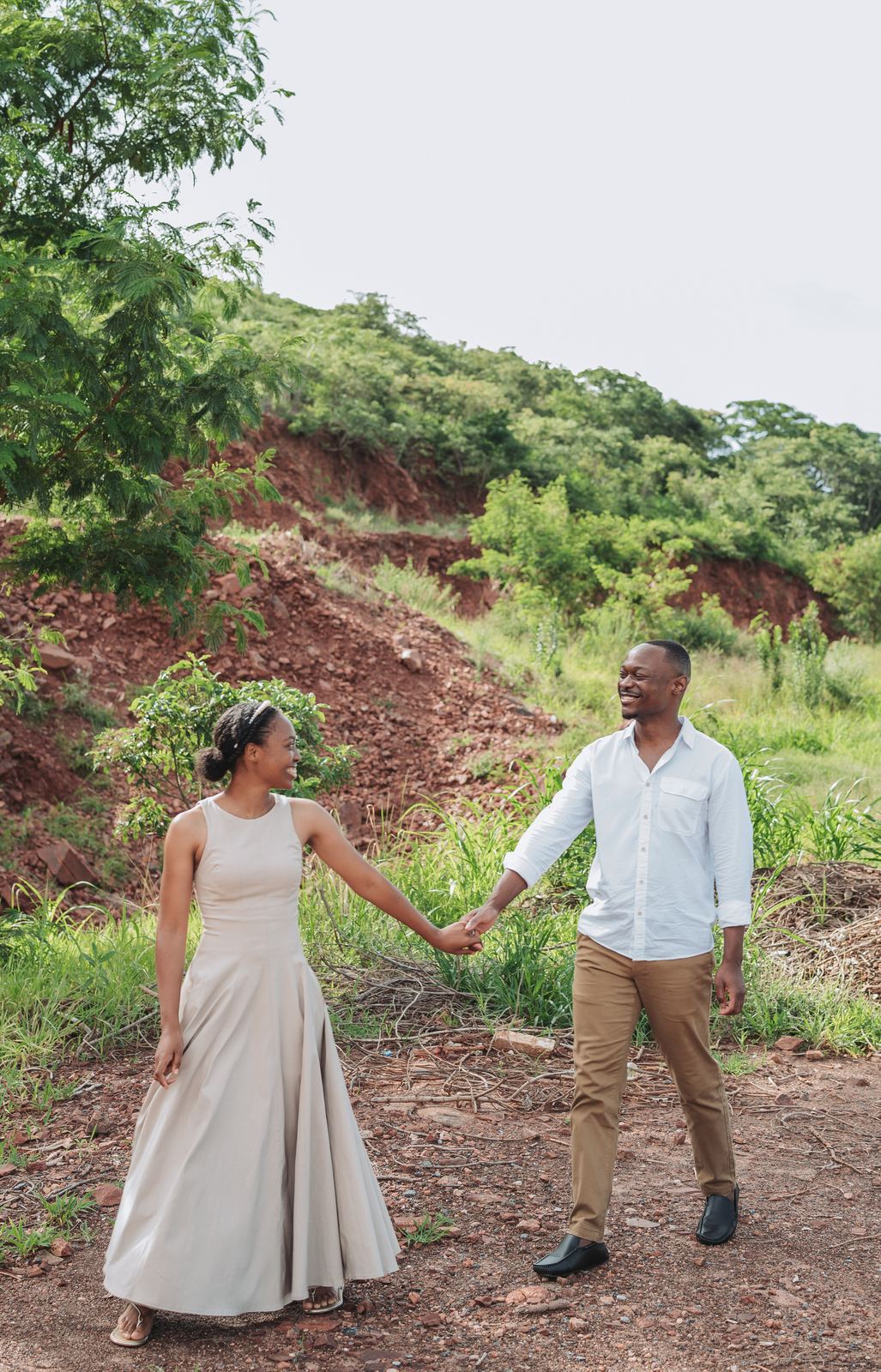 Charles and Shoma walking hand in hand along a red-earth path
