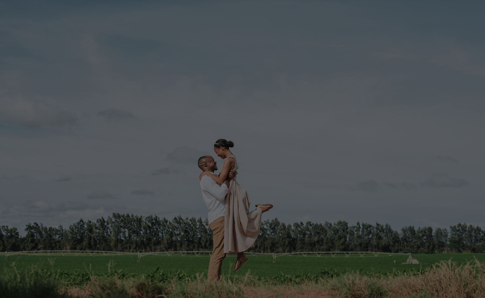Charles lifting Shoma in a green field under a stormy sky