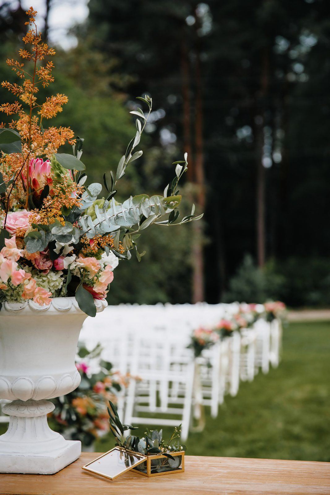 An aisle of white chairs beside a tall urn of peach, pink and white flowers