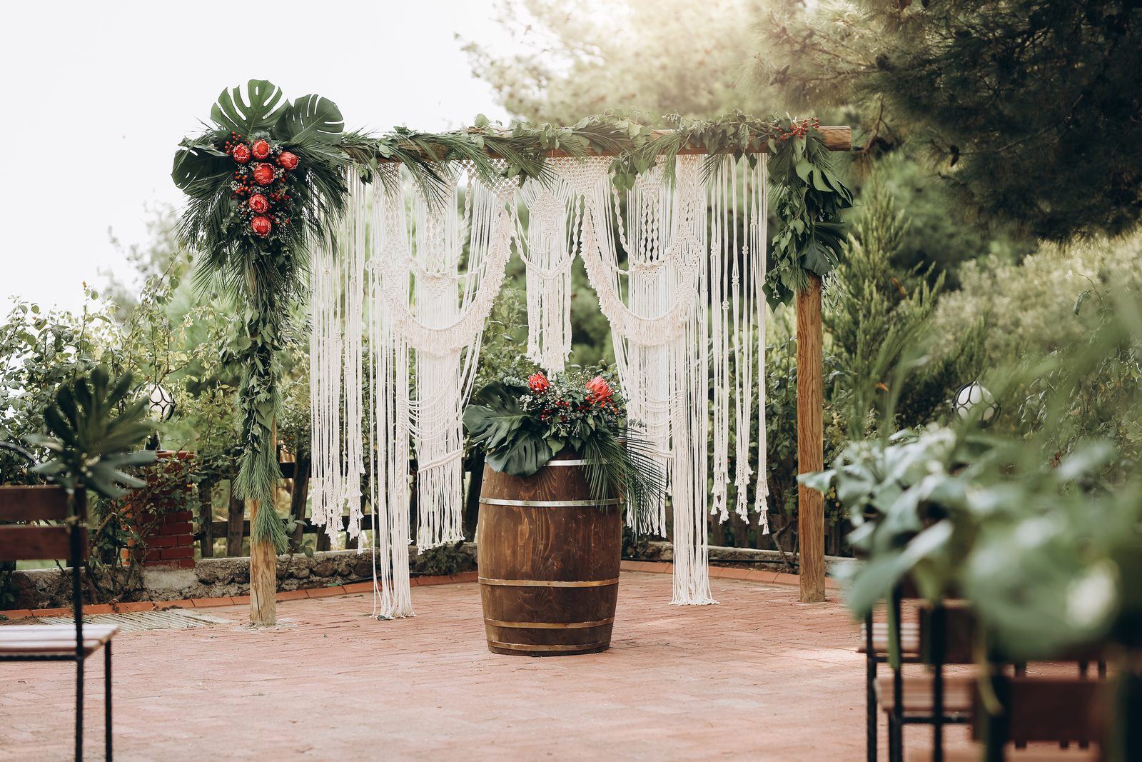 A macramé wedding arch with tropical flowers beside a wooden barrel